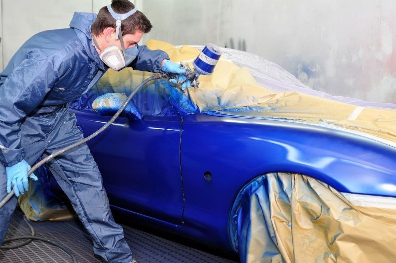 Мастер наносит синюю краску на авто из распылителя
